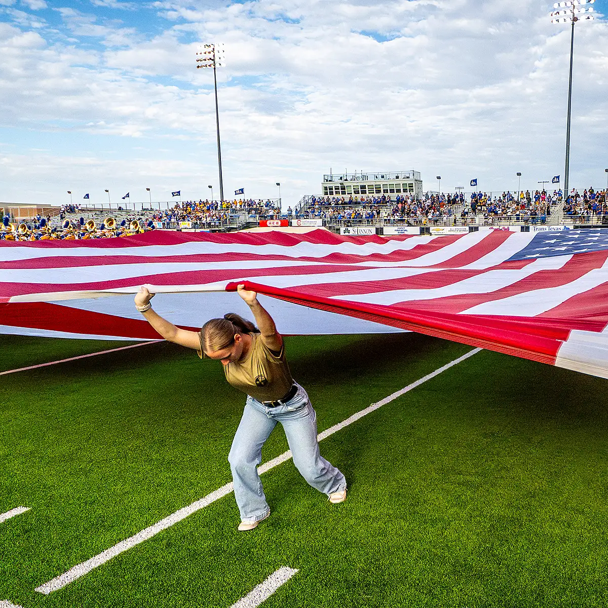 ASU Military Student pulls large U.S. Flag across football field to celebrate military appreciation day.